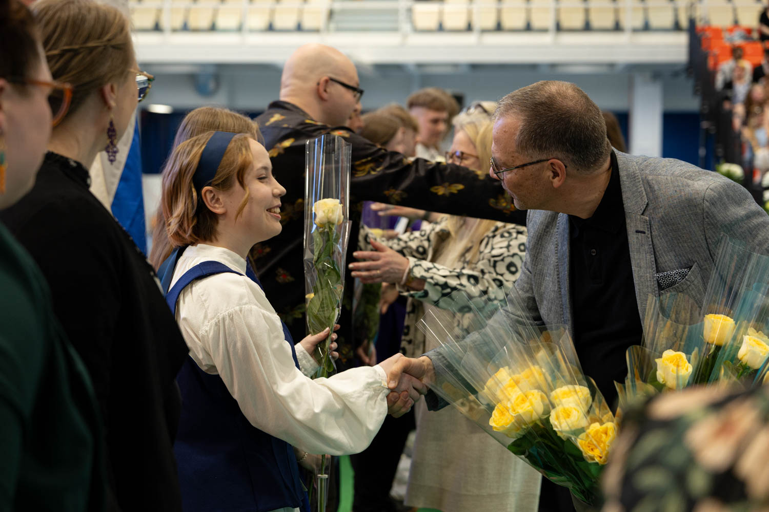 Opiskelija ottaa vastaan kukan ja kättelee valmistujaisissa.